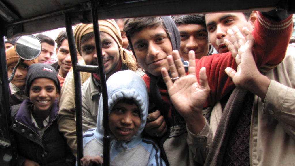 Crowds of people look through the window of the rickshaw. Some are waving and leaning in.