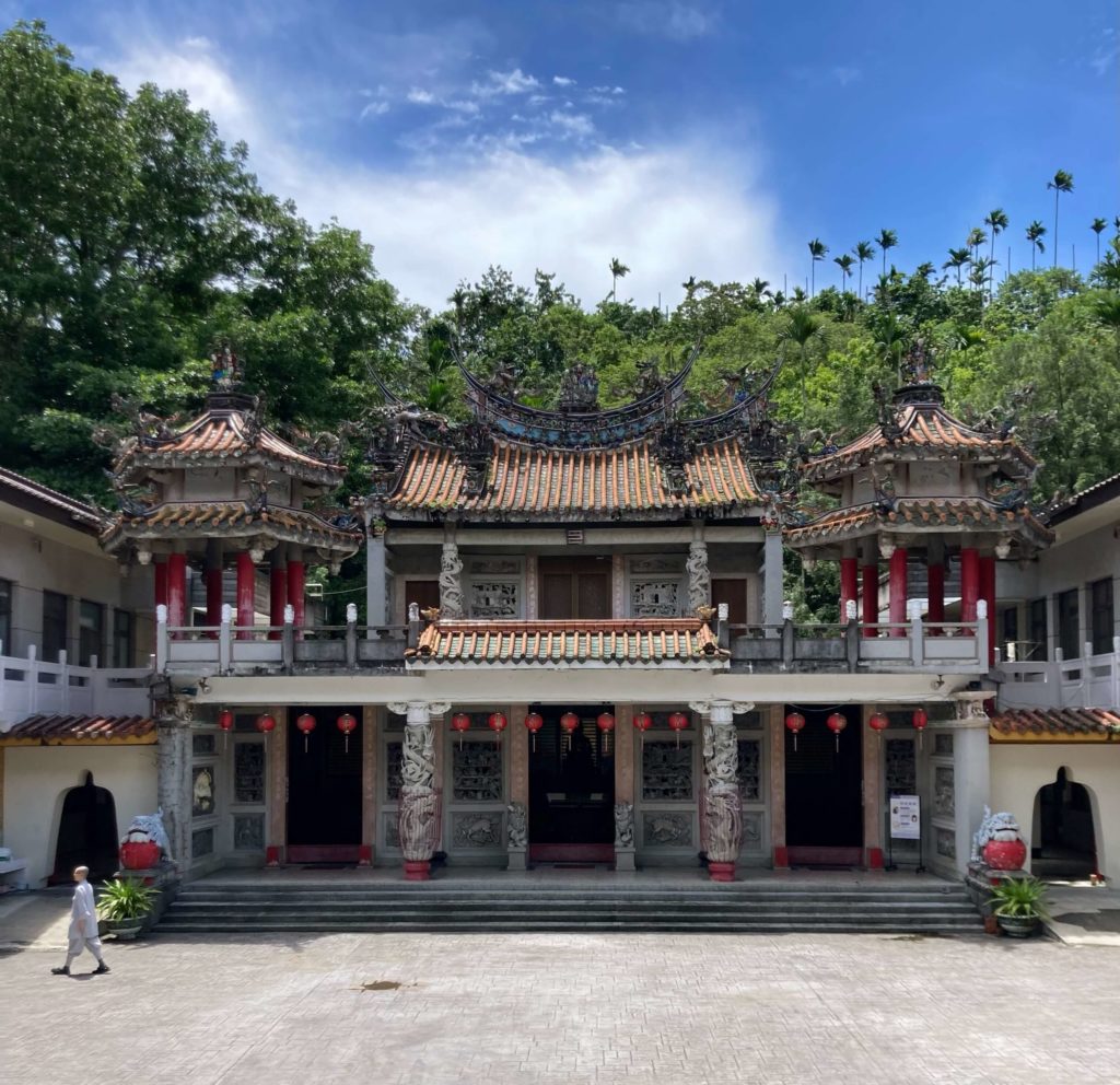 Xiang Guang (Incense Light) Temple. The temple is ornate, decorated mainly in red and white. Red lanterns hang in front of the temple. The temple is surrounded by trees.
A nun walks past the building. 