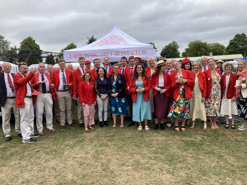 Lots of people in red LMBC blazers stand on the grass in front of the LMBC gazebo.
