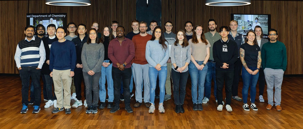 Members of the Reisner Laboratory standing in front of a panelled wall in the Department of Chemistry.