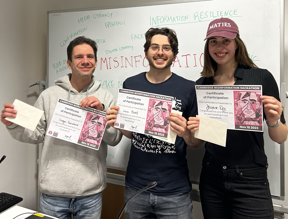 Josie and her teammates pose with their certificates in front of a whiteboard. Josie wears a burgungy baseball cap.