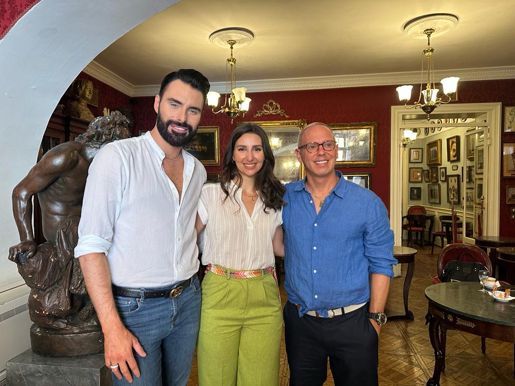 Tatyana stands with her arms around Rylan Clark and Rob Rinder from BBC's 'Rob and Rylan’s Grand Tour'. They are in Antico Caffè Greco and lots of works of art and mirrors adorn the wall behind them.