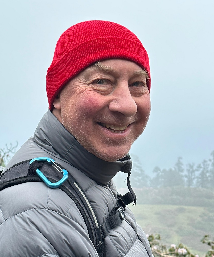 A head and shoulders shot of Chris Perks. He is wearing a dark grey puffy coat and a read beanie.