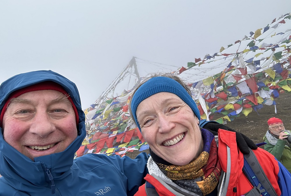 This is a selfie of Chris and his wife wearing hiking gear. In the background are lots of small flags in red, blue, yellow, green and white.