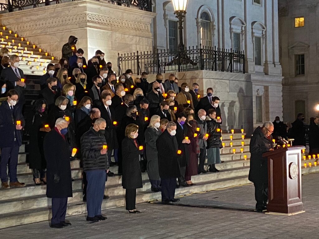 People line the steps. They are all wearing dark clothes and face masks and are holding candles. 