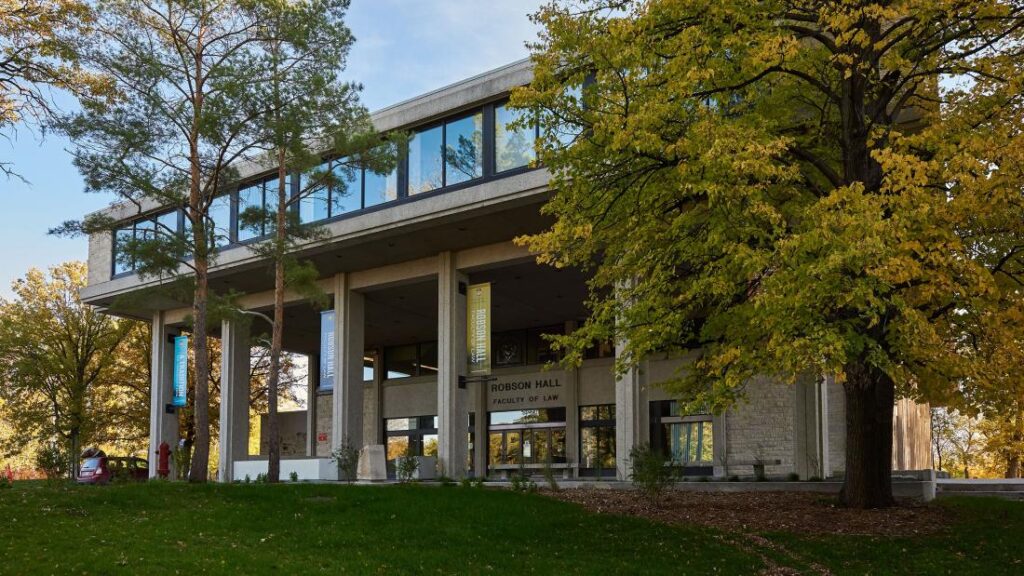 A two-story concrete building with large windows, surrounded by trees with autumn foliage. It has the name 'Robinson Hall, Faculty of Law' on it.